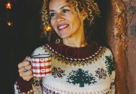 Photo for Horizontal portrait of attractive middle age woman smiling and taking tea cup in Christmastime at home. Happy female people enjoy xmas holiday celebration. Copy space image for December month - Royalty Free Image