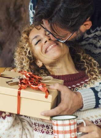 Photo for Happiness and love people in christmas gift exchange leisure activity at home. Man giving a surprise present to an overjoyed and excited woman sitting on the sofa. Winter holiday celebration indoor - Royalty Free Image