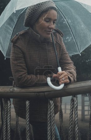 Téléchargez les photos : Femme sous la pluie protégée par un parapluie transparent profiter de mauvaises conditions météorologiques pluvieuses romantiques en automne hiver activité de loisirs de plein air seul. Romance et portrait de femmes. Dame solitaire - en image libre de droit
