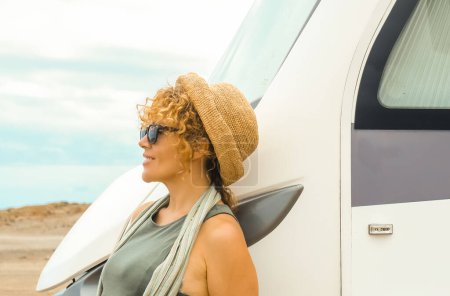 Photo for Traveler independent woman standing outside her modern motorhome tiny house camper van and admiring the scenic parking destination. Concept of nomadic lifestyle and female people alone. Travel - Royalty Free Image