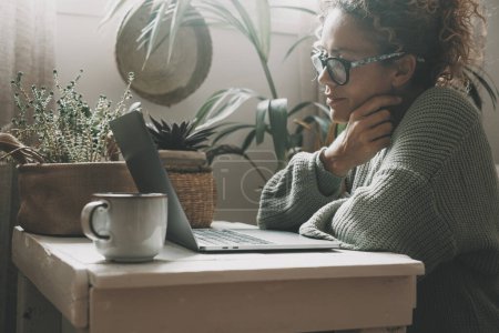 Téléchargez les photos : Femme écrivant sur ordinateur portable à la maison dans le jardin intérieur vert lieu de travail. Les gens et la technologie. Concept de mode de vie sain et moderne, féminin. Loisirs intérieurs en ligne. Surfer sur le net - en image libre de droit
