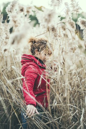 Photo for Woman walking in the high grass field outdoors wearing red jacket. October winter autumn season and people in outdoor leisure activity enjoying nature and lifestyle. Freedom and connection outside - Royalty Free Image