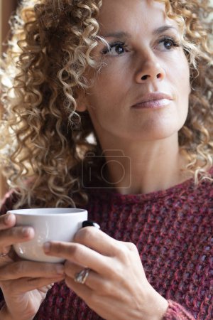 Photo for Serene people concept lifestyle. woman drinking coffee or healthy beverage tea alone near the window at home looking outside and thinking. Dreamer female enjoy time at home. Relaxed young lady - Royalty Free Image