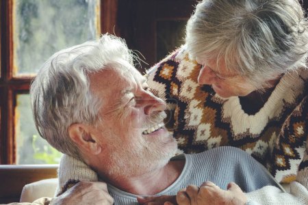 Photo for Happy senior couple hug and enjoy time together at home sitting on the chair and smiling each other. Concept of old people mature relationship. Joy retired life for old man and woman in winter life - Royalty Free Image