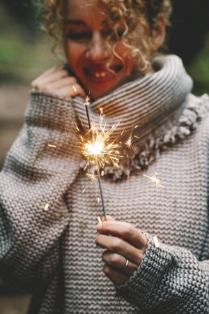 Photo for Happy woman celebrating outdoor with sparkler fire and smile. Concept of people and celebration. Birthday and new year eve. One female alone enjoys life in autumn. Green background nature - Royalty Free Image