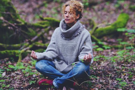 Foto de Mujer de estilo de vida saludable sentada en el suelo en posición de yoga de loto con bosques verdes de la naturaleza alrededor. Mujeres y actividades de meditación zen al aire libre. Personas y conexión con la naturaleza - Imagen libre de derechos