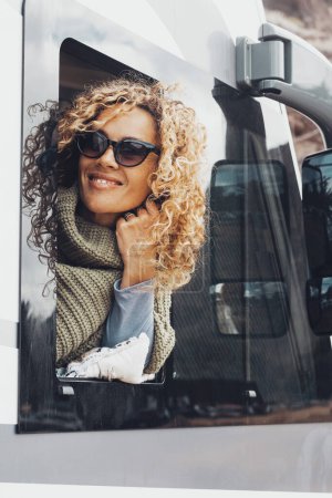 Foto de Mujer turística sonrisa fuera de la ventana caravana llegó a destino. Alternativa de camping coche de viaje estilo de vida y vacaciones. Vanlife gente nómada moderna. Jovencita en jornada de ocio - Imagen libre de derechos