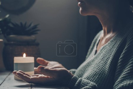 Foto de Mujer en casa en la actividad de meditación zen y la luz de las velas en el fondo. Una mujer con las manos en alto ora o medita sola en interiores de luz oscura. Concepto de estilo de vida mental saludable. - Imagen libre de derechos