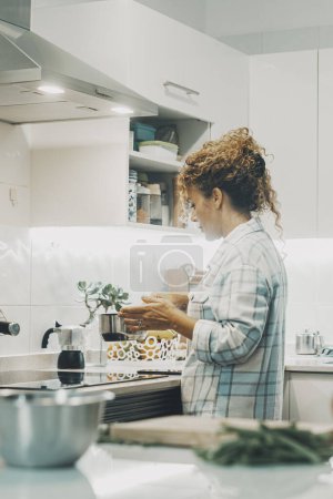 Photo for Woman cooking at home in the kitchen alone. Real single lifestyle for independent female people. Housewife preparing lunch for the family. View of lady using pot and prepare food indoor life. - Royalty Free Image