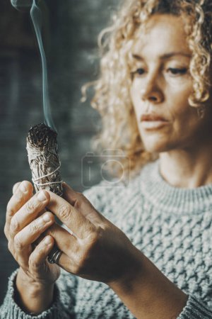 Photo for Portrait of a woman using a palo santo herbal incense to purify air and for spiritual leisure activity at home. Female people purify indoor house smoke burning wood. Concept of zen and spirituality - Royalty Free Image