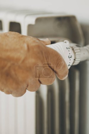 Photo for Close up of old man hand closing  heating home thermostat for gas energy saving. Concept of bills and heat crisis costs. People adjusting radiator supply to save money during winter - Royalty Free Image