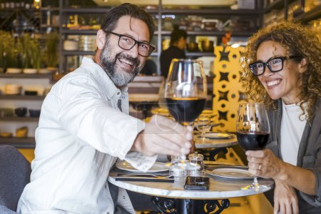 Téléchargez les photos : Couple heureux souriant et parlant dans un restaurant buvant du vin rouge - Couple marié déjeunant au café-bar - Concept de style de vie avec un homme et une femme sortant le week-end - en image libre de droit