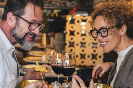 Téléchargez les photos : Couple heureux souriant et parlant dans un restaurant regardant le téléphone portable - Couple marié profiter de la pause déjeuner au café-bar - Les gens et le concept de la technologie - en image libre de droit