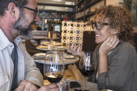 Photo for Happy couple smiling and talking in a restaurant drinking red wine - Married couple having lunch break at cafe bar - Lifestyle concept with man and a woman going out on weekend day - Royalty Free Image