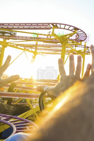 Téléchargez les photos : Couple sur un montagnes russes avec les bras en l'air amusé et excité attendant la descente raide. Après-midi ensoleillé avec plaisir. Concept de temps libre et de gaieté - en image libre de droit
