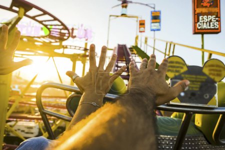 Couple on a roller coaster with arms in the air amused and excited waiting for the steep descent. Sunny afternoon with fun. Concept of free time and cheerfulness