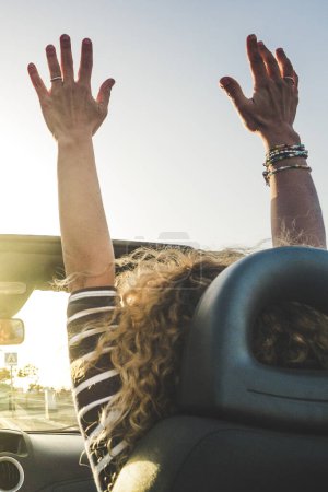 Foto de Mujer estilo de vida feliz disfrutar de los viajes con coche convertible bailando y conduciendo en la puesta del sol - concepto de ocio alegre viaje actividad de transporte para amigos personas divirtiéndose juntos - vacaciones de verano - Imagen libre de derechos