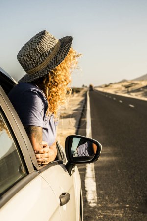 Foto de Tourist enjoy sun and outdoors outside the window of the car during a break. Vehicle parking on the side of the road and woman people admiring landscape. Concept of travel and summer holiday vacation - Imagen libre de derechos