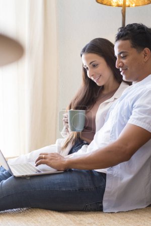 Photo for Young boy and girl together at home enjoying laptop computer sitting on the floor smiling and laughing - new life married people in love and relationship have fun watching online internet web - Royalty Free Image
