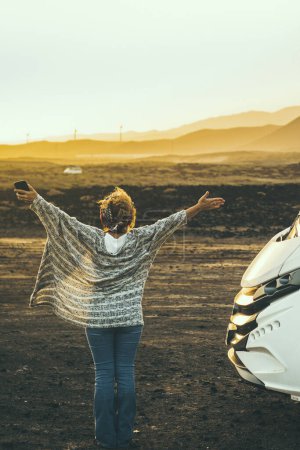 Photo for Woman viewed from back enjoy happy her destination in campe van life travel. Back view of female people opening arms and enjoy sunset landscape and freedom. Independence and alternative home vehicle - Royalty Free Image
