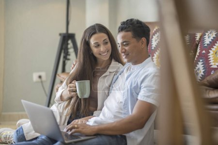 Téléchargez les photos : Jeune couple déménageant dans une nouvelle maison détente assis sur le canapé à l'aide d'un ordinateur portable, souriant heureux de déménager dans un nouvel appartement - en image libre de droit