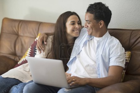 Photo for Young couple moving to a new home relaxing sitting on the sofa using computer laptop, smiling happy for moving to new apartment - Royalty Free Image