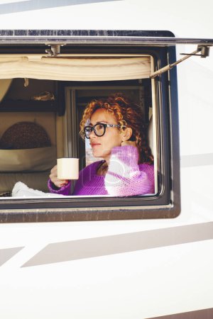 Foto de Mujer bebiendo café mirando por la ventana de una caravana - Imagen libre de derechos