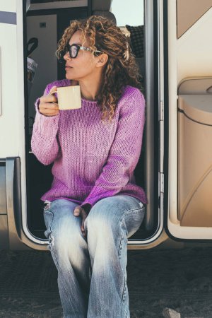 Téléchargez les photos : Femme buvant du café assis à la porte d'un camping-car - en image libre de droit