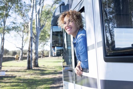 Téléchargez les photos : Belle femme bouclée caucasienne souriante penchée par la fenêtre d'un camping-car. Concept voyage, nature et loisirs - en image libre de droit