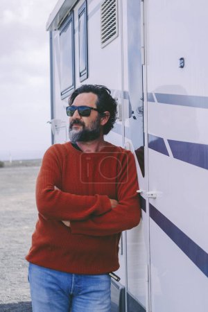 Téléchargez les photos : Man standing outside camper van in travel holiday vacation. Renting rv vehicle and enjoy freedom. Mature people with motor home. Off grid alternative house concept. Adult male with beard - en image libre de droit