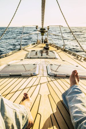 Foto de Pov punto de vista de las piernas del hombre que pone y se relaja en la cubierta del barco de vela de madera solo con puesta de sol en el fondo - concepto de personas de viaje y la libertad en vacaciones de verano - Imagen libre de derechos