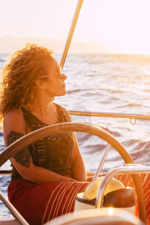 Foto de Mujer viajando en barco al atardecer entre los océanos: felices y libres vacaciones de estilo de vida alternativo moderno, las mujeres navegan al atardecer con el océano y el sol de fondo. - Imagen libre de derechos