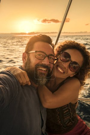 Photo for Happy couple of tourist take selfie and smile enjoying the summer sunset in holiday vacation - yacht luxury lifestyle people - sunlight in background and blue ocean - Royalty Free Image