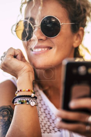 Foto de Retrato de hermosa mujer adulta uso de teléfono inteligente celular y sonriente - moderno de moda alegre mujer caucásica personas disfrutan y hacen videollamada - pulseras accesorios - Imagen libre de derechos