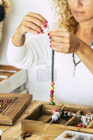 Photo for Woman at home make handmade jewelry. Box with beads on old wooden table. view with woman hands - tutorial to learn how to make bracelets and jewelry online and alternative home job - Royalty Free Image