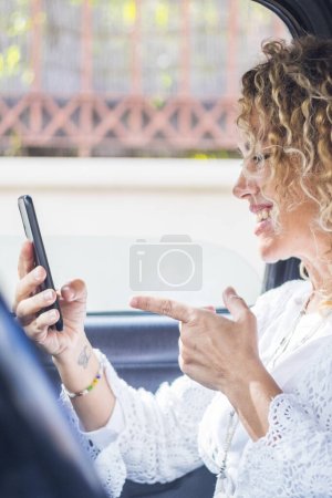 Foto de Mujer adulta feliz haciendo videollamadas sentado dentro del coche - la gente utiliza la tecnología en línea durante el transporte - viajar femenino y el concepto de móvil itinerante - mujer alegre hablar en el teléfono celular - Imagen libre de derechos