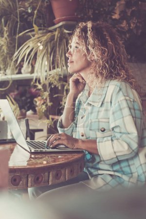 Photo for Woman work at home in smart working job with laptop computer sitting on the table and looking outside the window - happy adult woman smile and enjoy online modern lifestyle - Royalty Free Image