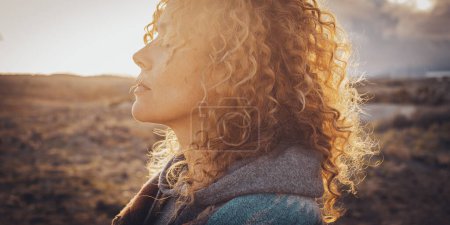 Photo for Side portrait of beautiful middle age blonde woman with long curly hair and closed eyes enjoying sunset in outdoors travel leisure activity alone. Wanderlust and interior balance happiness and freedom - Royalty Free Image