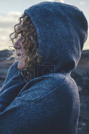 Photo for Woman hugging herself with love and care and smile looking enjoying scenic destination travel place. Sky in background, Hood on head. Concept of freedom and traveler lifestyle people female - Royalty Free Image