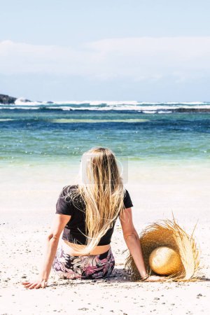 Photo for Back rear view of blonde long hair woman sit down on the sand - Royalty Free Image