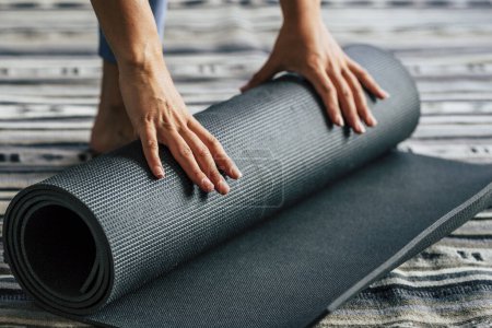 Foto de Yoga en casa estilo de vida activo mujer rodando alfombra de ejercicio en la sala de estar para la meditación matutina concepto de yoga fondo - personas sanas en el deporte diario ejercicio actividad física - Imagen libre de derechos