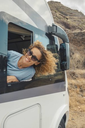 Téléchargez les photos : Happy and free single woman smiling and enjoying the destination outside the window of her camper van. Concept of renting rv motor home vehicle to travel in holiday vacation. Van life and off grid house - en image libre de droit