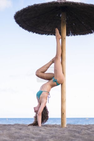 Téléchargez les photos : Belle brune mince faisant du yoga position d'exercice inverse à la plage dans l'entraînement en plein air - en image libre de droit
