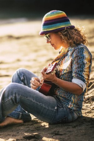 Téléchargez les photos : Femme s'asseoir à la plage jouer de la guitare profiter des loisirs de plein air d'été en vacances Voyage seul concept de femme indépendante profiter du monde voyager et jouer de la musique - en image libre de droit