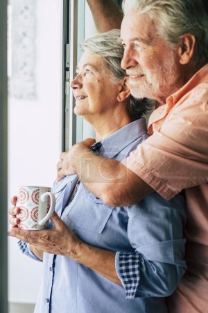 Téléchargez les photos : Heureux couple mature âgé tendrement amoureux à la maison regardant par la fenêtre de la porte concept de personnes âgées ensemble pour toujours homme et femme à l'intérieur - en image libre de droit