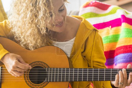 Photo for Adult caucasian woman playing acoustic guitar at home sitting on the sofa and smiling with fun - female people with music hobby leisure activity indoor - lady learning to touch guitar cords and enjoy singer lifestyle - Royalty Free Image