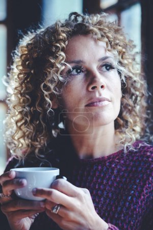 Téléchargez les photos : Portrait de femme adulte séduisante réfléchie à la maison tenant café - en image libre de droit