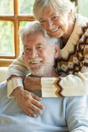 Téléchargez les photos : Happy and enjoyed senior caucasian couple smile and hug each other sitting on a chair in cozy home cabin chalet - two man and woman old elderly people lifestyle enjoying relax and relationship - en image libre de droit
