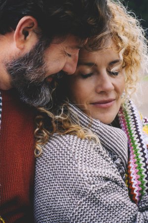Téléchargez les photos : Couple adulte romantique rester ensemble avec le sentiment et l'amour couvert par une couverture colorée en laine au parc extérieur. Concept de vie de relation heureuse personnes. Saison de loisirs d'hiver dehors - en image libre de droit