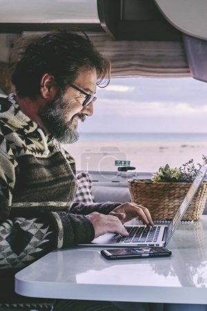 Photo for Adult man use laptop computer to work inside camper van with roaming phone connection. Concept of modern people lifestyle in smart working or travel digital nomad freedom - Royalty Free Image